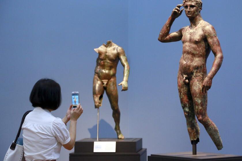 FILE - Reporter Sookee Chung takes a photo of a sculpture titled "Statue of a Victorious Youth, 300-100 B.C." at the J. Paul Getty Museum in Los Angeles, on July 27, 2015. A European court upheld Italy’s right to seize a prized Greek statue from the J. Paul Getty Museum in California, rejecting the museum’s appeal on Thursday and ruling Italy was right to try to reclaim an important part of its cultural heritage. (AP Photo/Nick Ut, File)