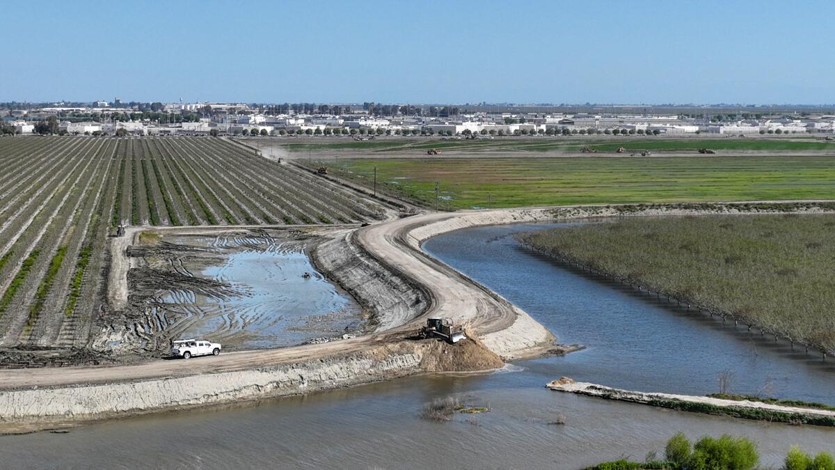 A broken levee along the Tule River, with vehicles working on it.
