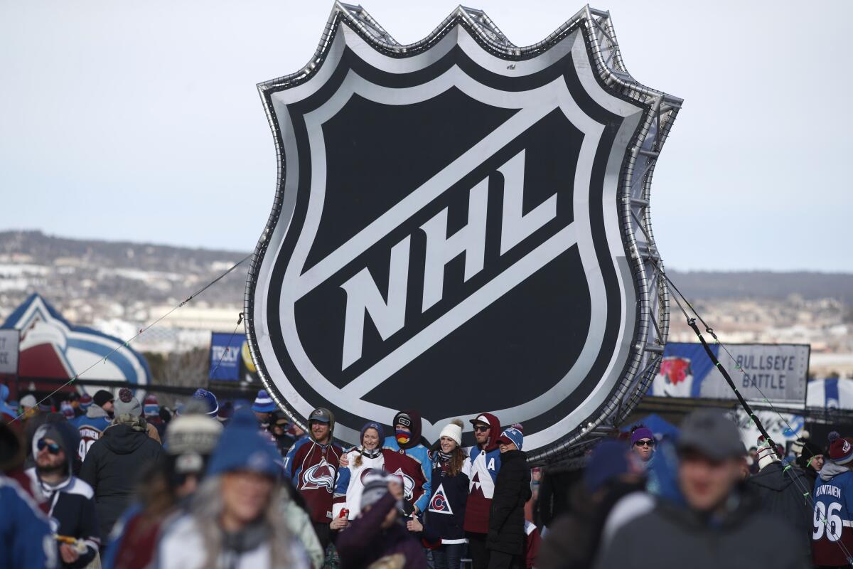 In this Feb. 15, 2020, photo, fans pose below the NHL logo outside Falcon Stadium before an outdoor game between the Kings and Colorado Avalanche in Colorado Springs, Colo.