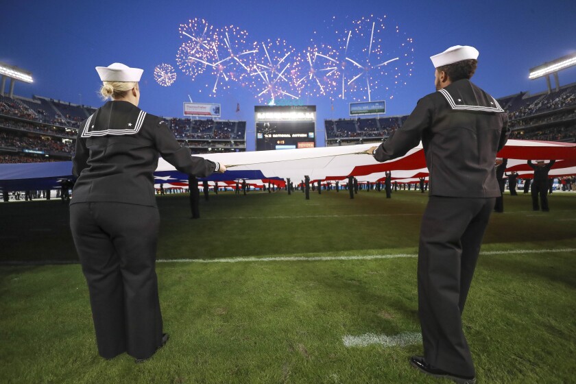 Members of the military holding a U.S. flag on a football field under fireworks