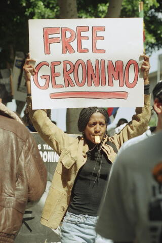 A woman holds a white sign with the words 'Free Geronimo' written in red
