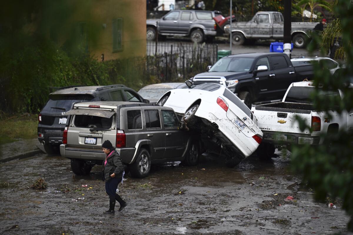 A woman walks by cars damaged from floods