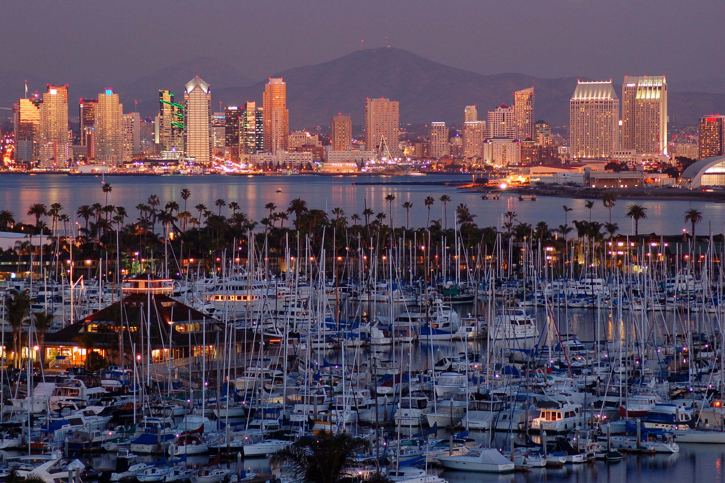 The sunset is reflected in the skyline and the calm marina of San Diego, California.