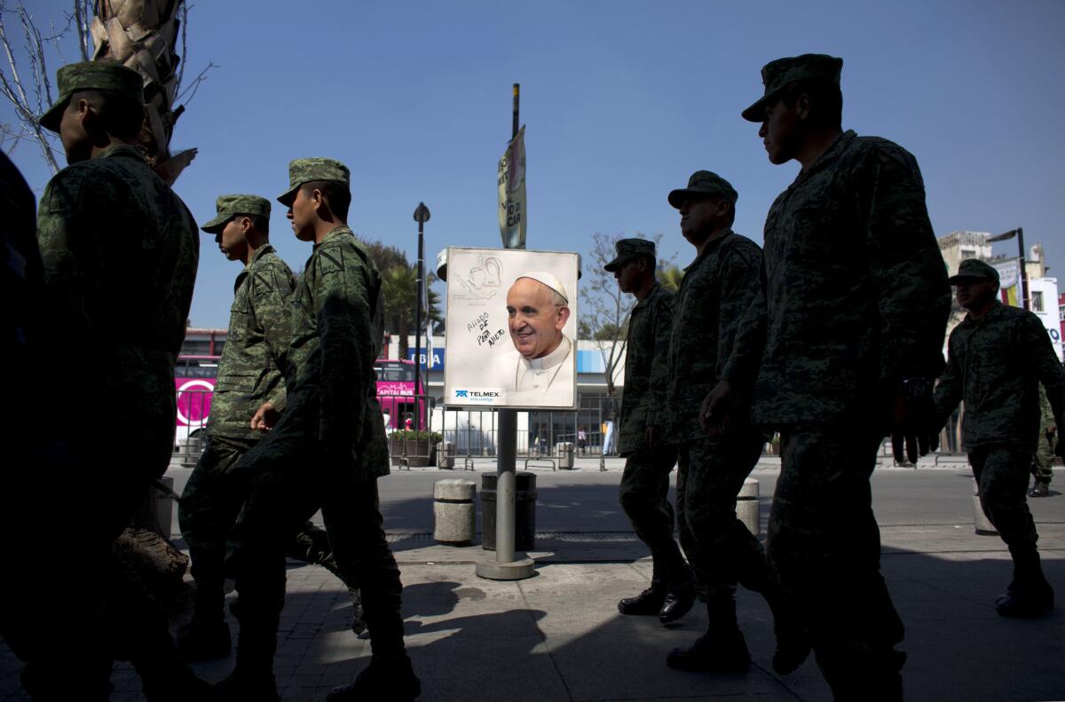 Soldiers walk past an image of Pope Francis on a phone booth in Mexico City.