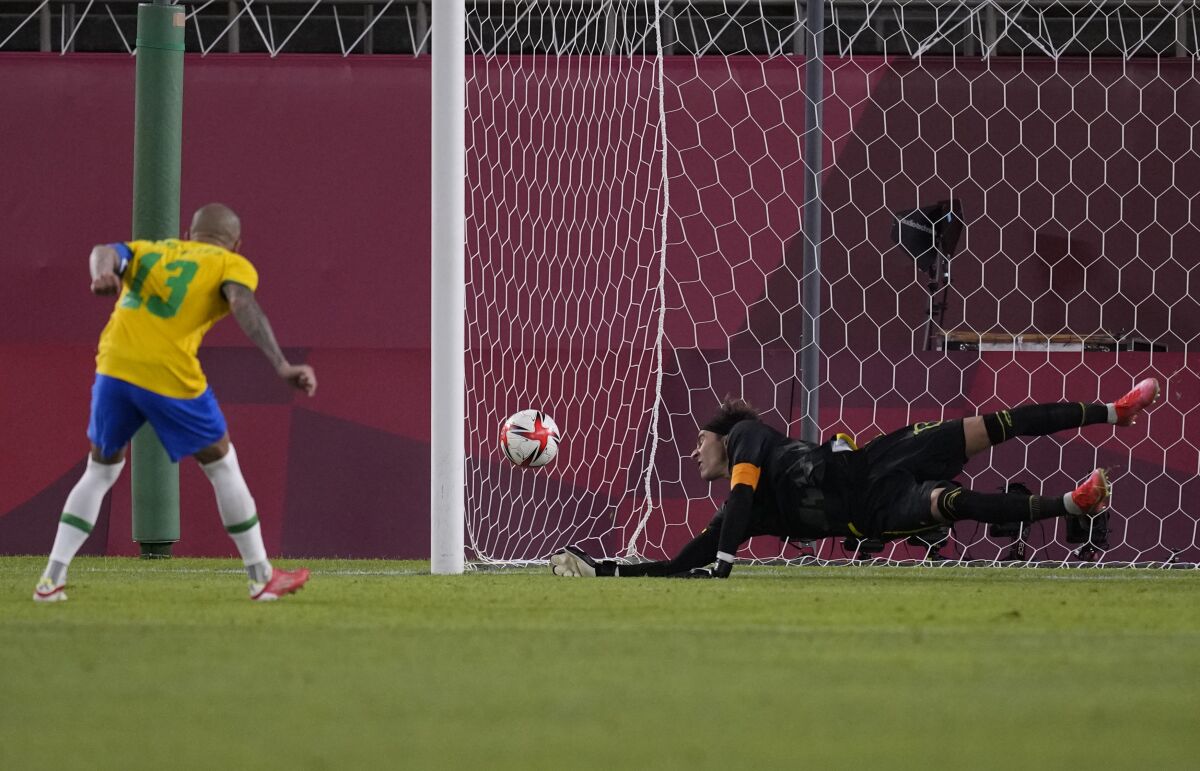 Guillermo Ochoa of Mexico tries to block a kick by Brazil's Dani Alves during men's soccer at the Tokyo Olympics.