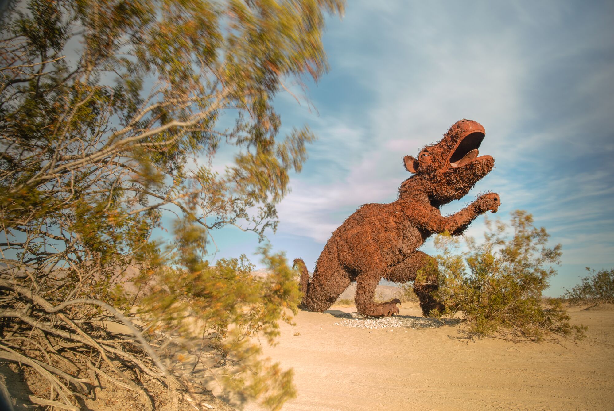 A metal sculpture of a creature standing in the desert.