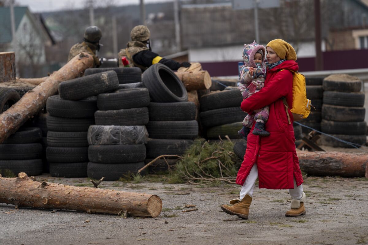 A Ukrainian woman holding a baby walks past a barricade controlled by Ukrainian soldiers as they flee crossing the Irpin river in the outskirts of Kyiv, Ukraine, Saturday, March 5, 2022. (AP Photo/Emilio Morenatti)