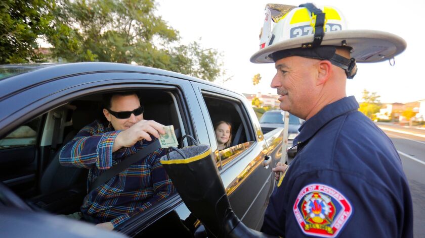 Jake Dupuy, left, drops a donation in the boot of Poway Fire Department Battalion Chief Brian Mitchell, right, at the intersection of Poway Road and Community Road Friday morning for the family of Cal Fire engineer Cory Iverson of Escondido who was killed on December 14th.