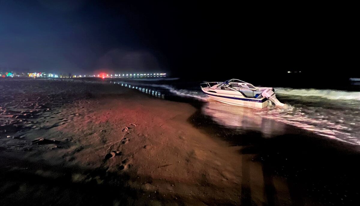 A small boat is seen at night on a sandy beach.