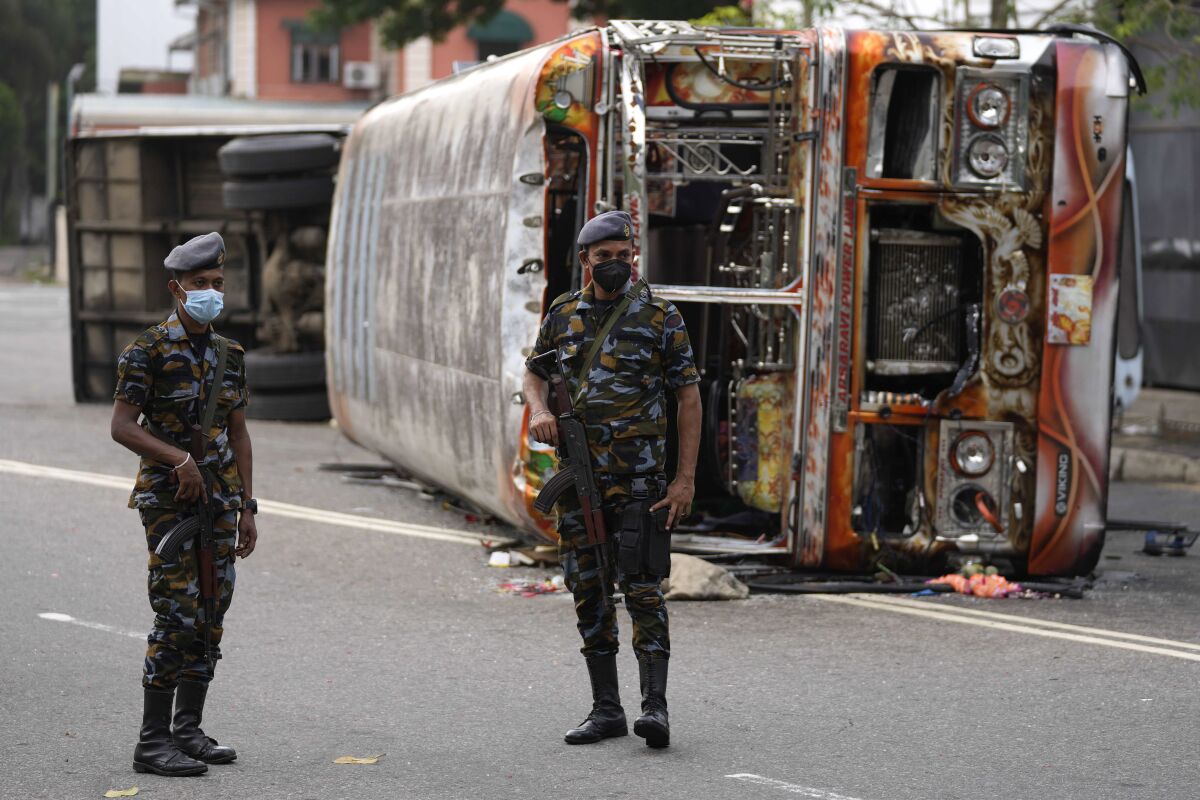 Sri Lankan soldiers stand guard next to burnt buses a day after clashes between government supporters and anti-government protesters in Colombo, Sri Lanka, Tuesday, May 10, 2022. Defying a nationwide curfew in Sri Lanka, several hundred protesters continued to chant slogans against the government Tuesday, a day after violent clashes saw the resignation of the prime minister who is blamed, along with his brother, the president, for leading the country into its worst economic crisis in decades. (AP Photo/Eranga Jayawardena)
