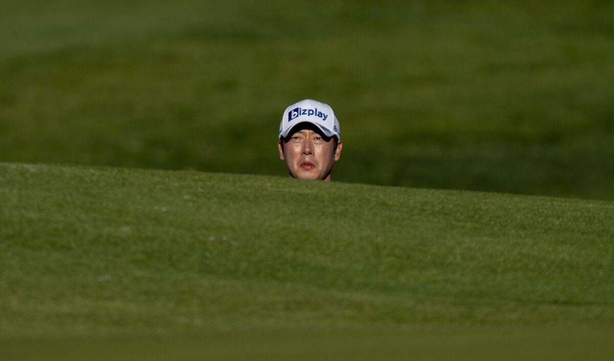 Tae Hoon Kim of South Korea peers out over a green side bunker to see where his ball lands on the second hole.