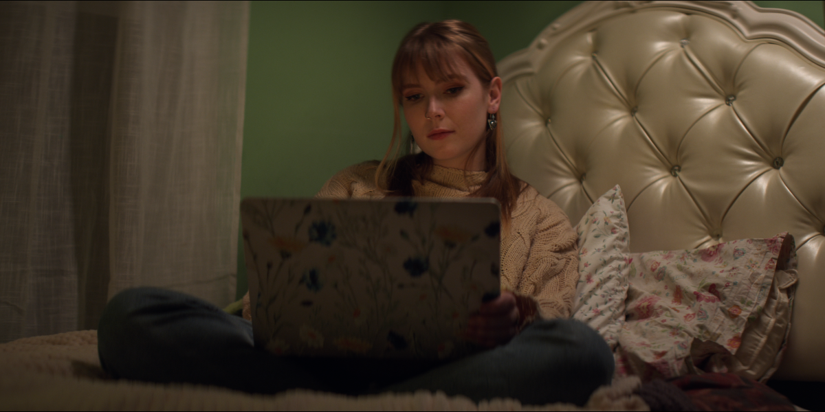 A young woman writing on a laptop on her bed.