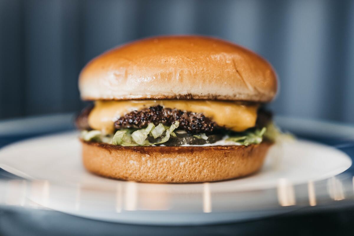A closeup photo of a single Trophies cheeseburger against dark blue tile. 