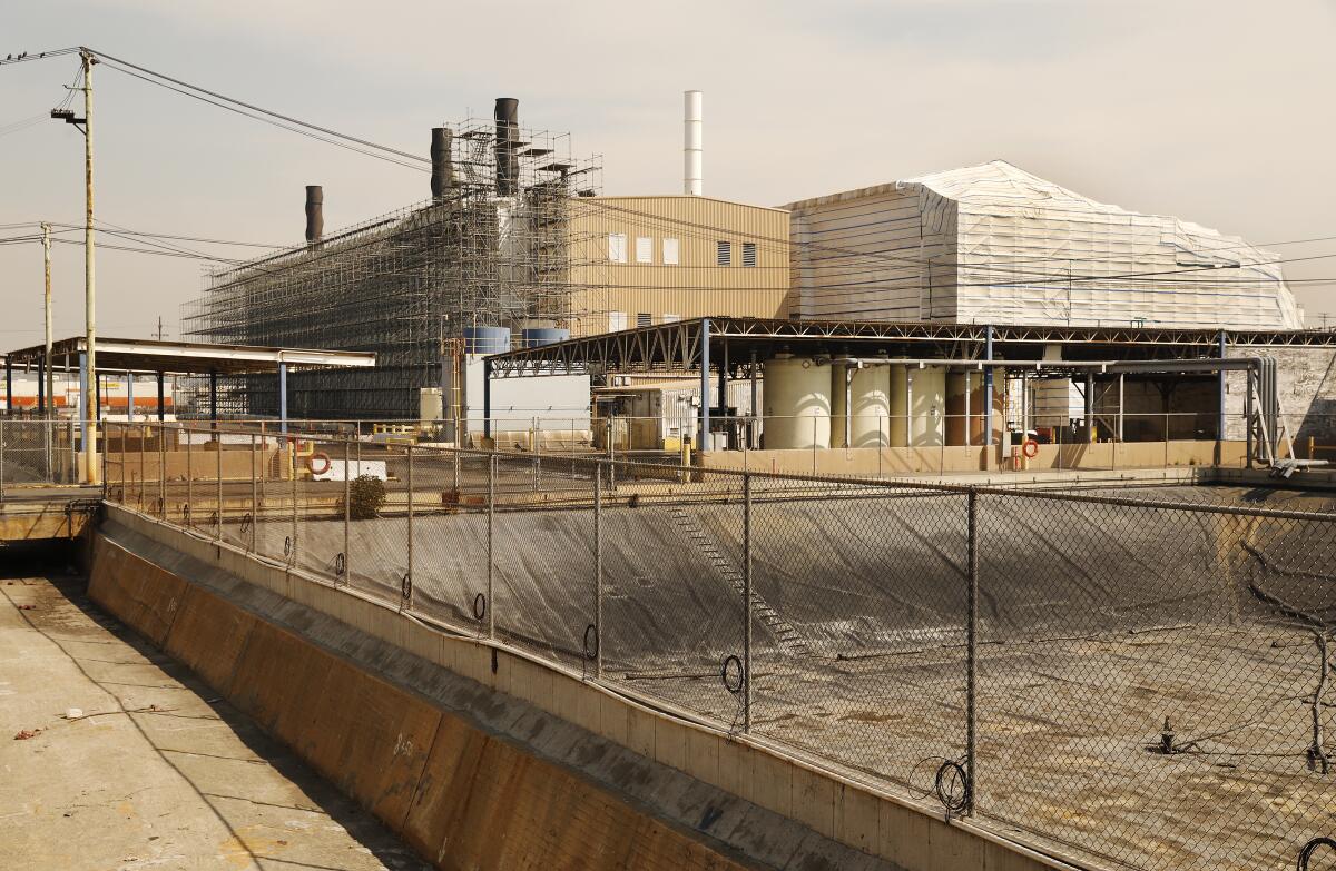 An industrial facility rises from behind a chain link fence.