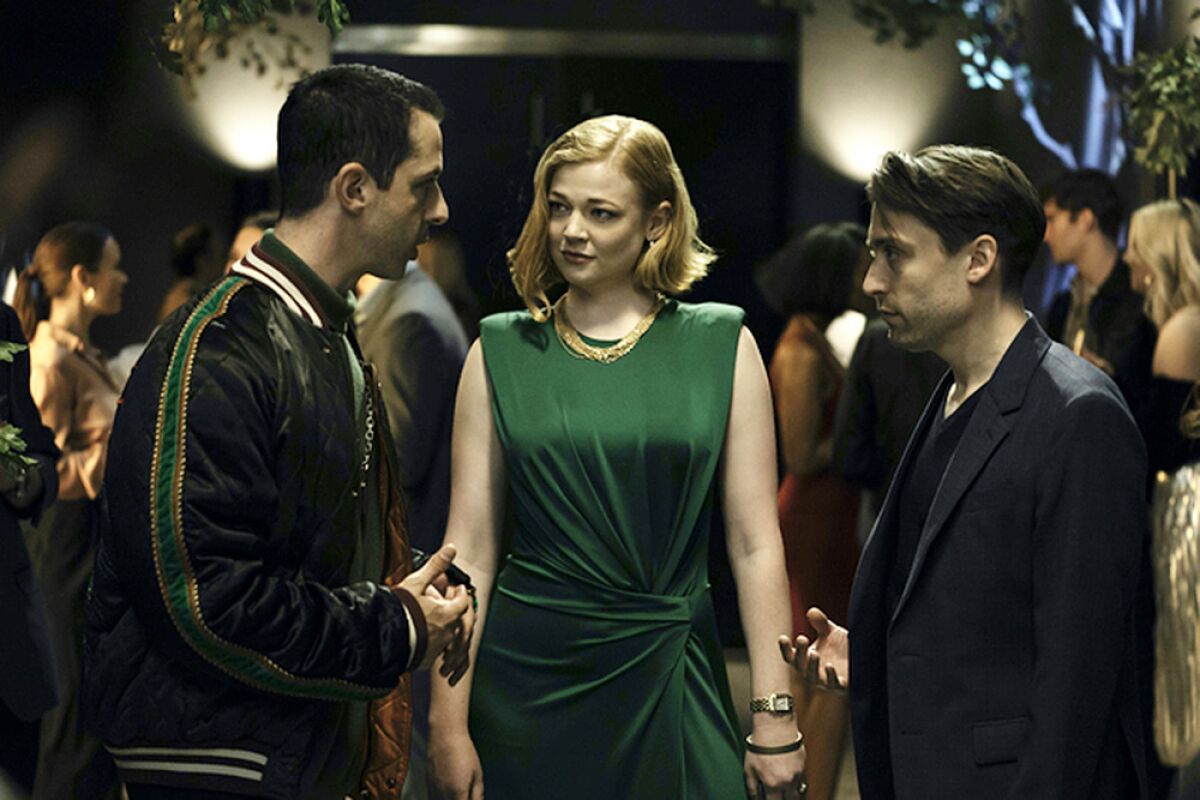 Two men and a woman in a green dress stand together at a party.