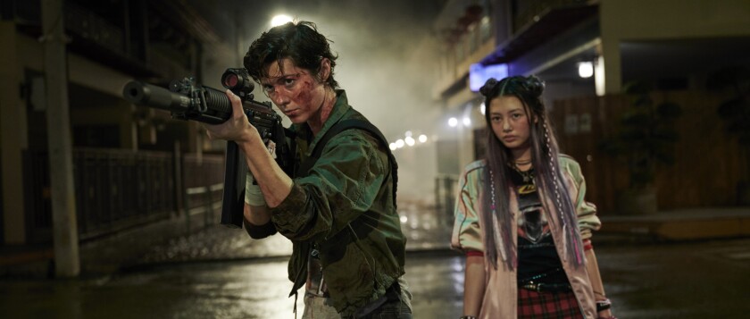 A bloodied woman aims a firearm as a younger woman watches in the movie "Kate."