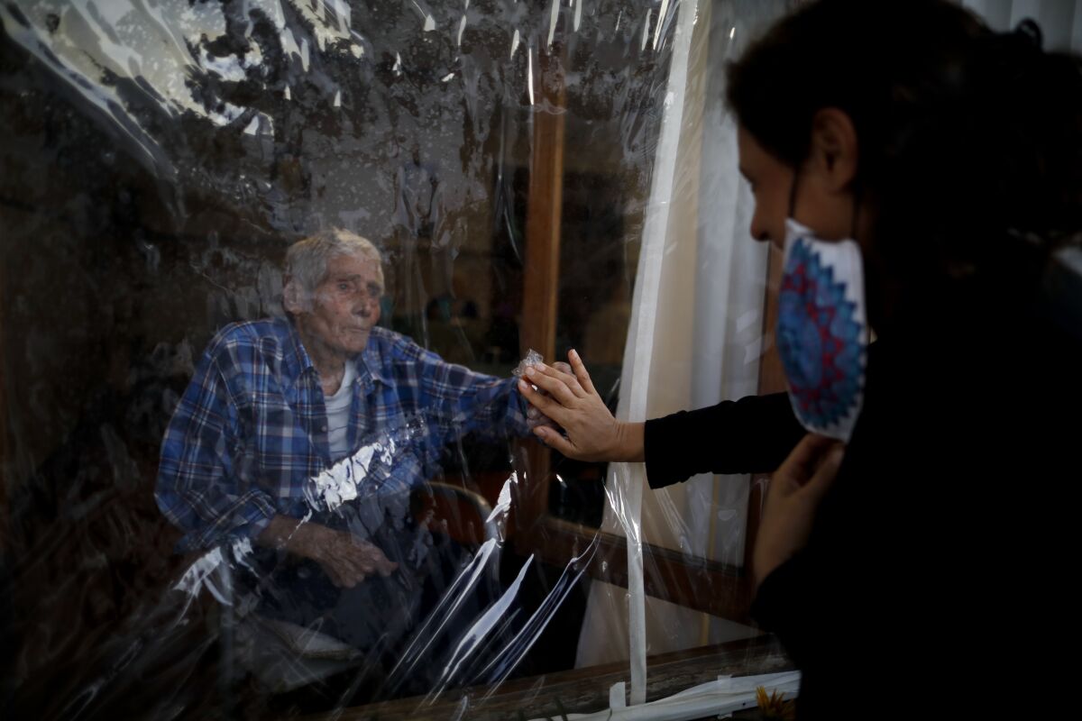 Victor Tripiana, 86, reaches out to touch the hand of his daughter-in-law, Silvia Fernandez Sotto, separated by a plastic sheet to prevent the spread of COVID-19, at the Reminiscencias residence for the elderly in Tandil, Argentina, on April 4, 2021. (AP Photo/Natacha Pisarenko)