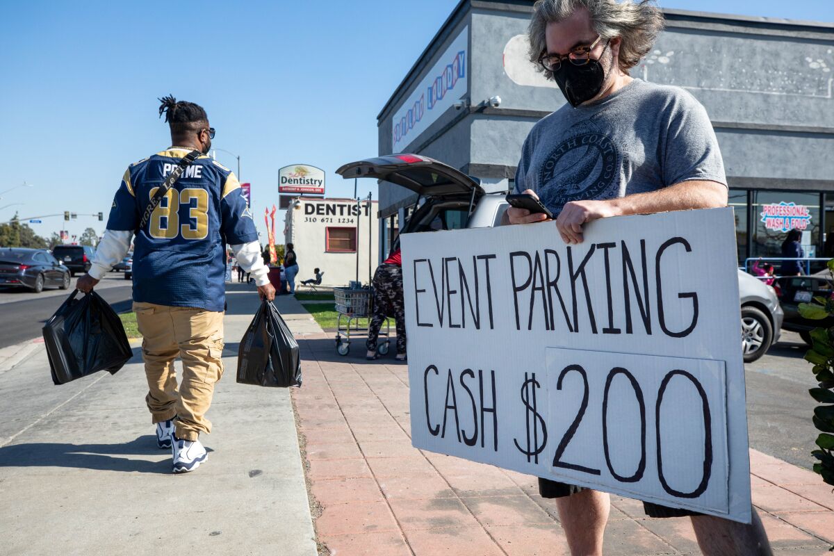 A man holds a sign that says event parking will cost $200 in cash.