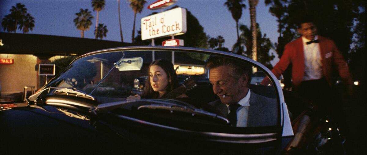 A man sits in the driver's seat and a woman in the passenger's seat of a car at night