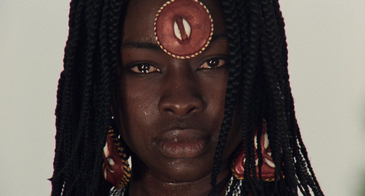 A woman with a forehead ornament stares into the lens.