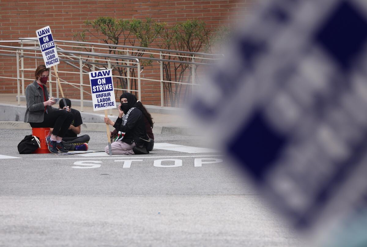 Striking workers sit in a driveway holding picket signs.