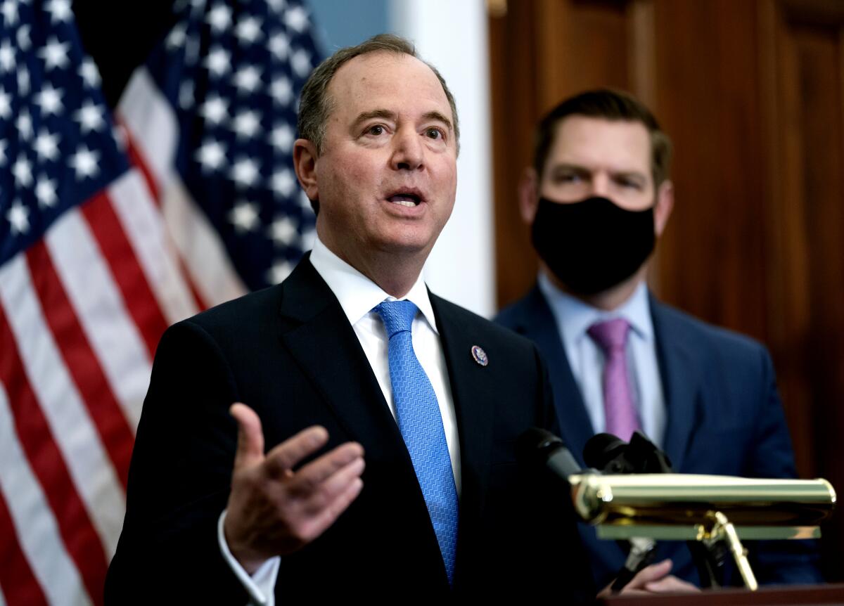 Adam Schiff speaks from behind a podium as Eric Swalwell stands to the side 