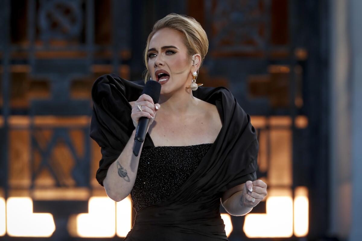 Adele, in a black dress, sings into a microphone.