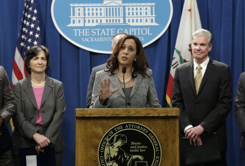 Kamala Harris speaks at a lectern as a group of colleagues stand behind her