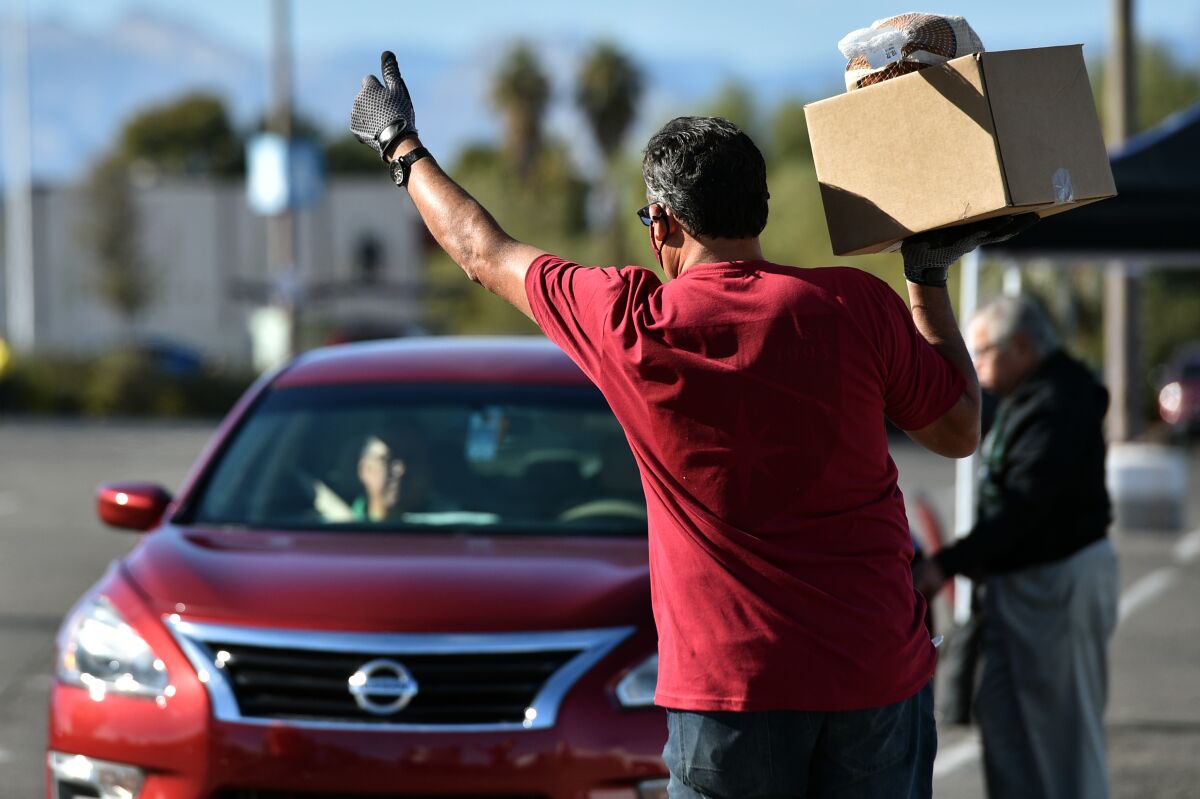 Greg Arce carries a Thanksgiving dinner for distribution during the Fall Giving Pop-Up as a car drives up.