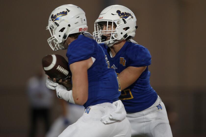 Fountain Valley High starter James Russell, right, hands the ball off to running back Tanner Ciok for a touchdown against Woodbridge during the first half in a nonleague game on Thursday at Huntington Beach High.
