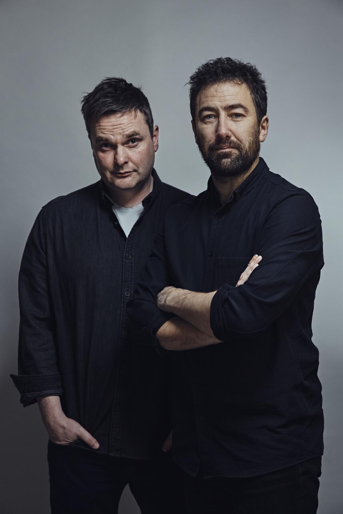 Two men in dark shirts and trousers posing for a photograph.