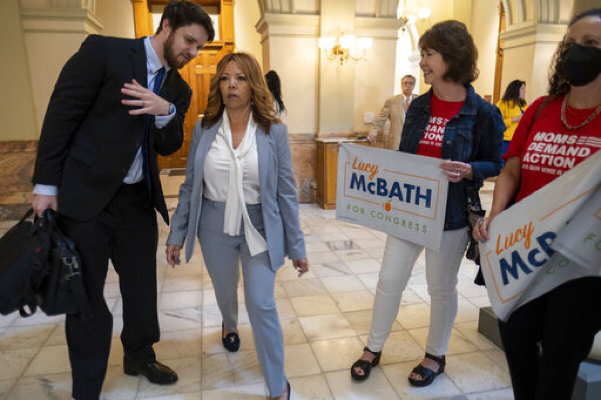 Rep. Lucy McBath, wearing a blue suit, speaks with a man as two women nearby hold signs supporting her reelection. 