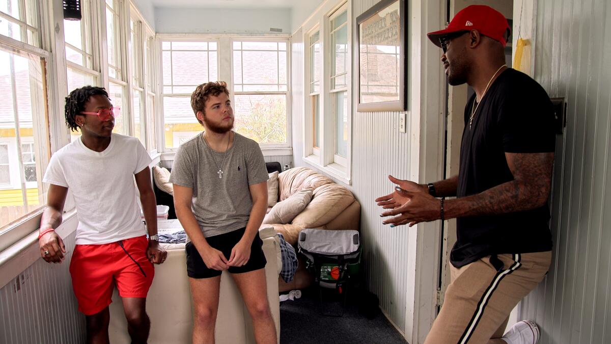 Two young men stand in their frat house with "Queer Eye's" Karamo Brown.