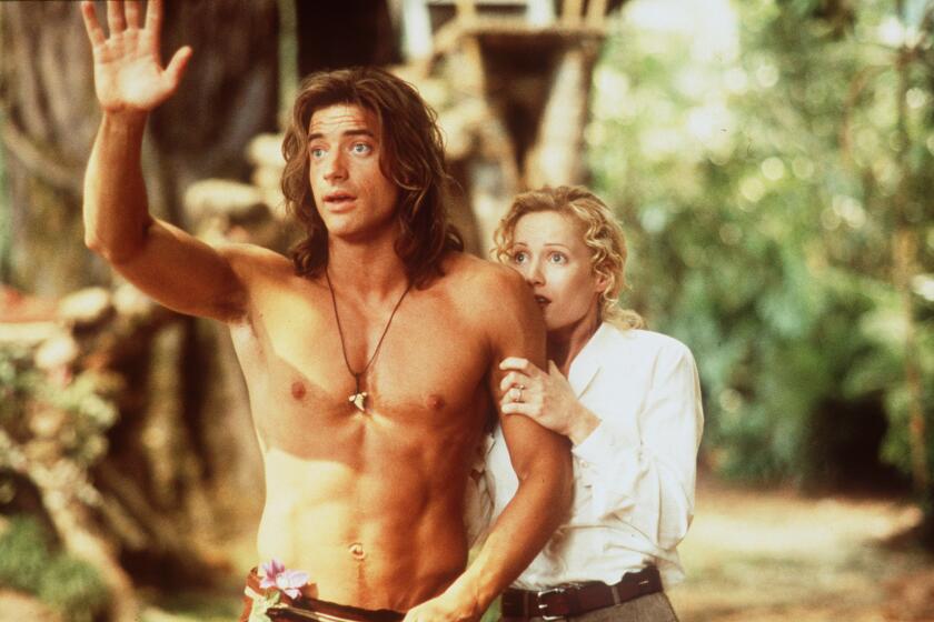 A blond woman in a white shirt clinging to a shirtless man with long brown hair who is waving