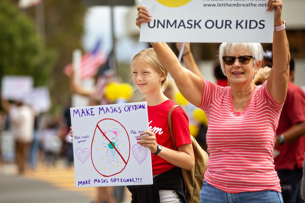 A woman and girl hold signs reading "Unmask our kids" and "Make masks optional."