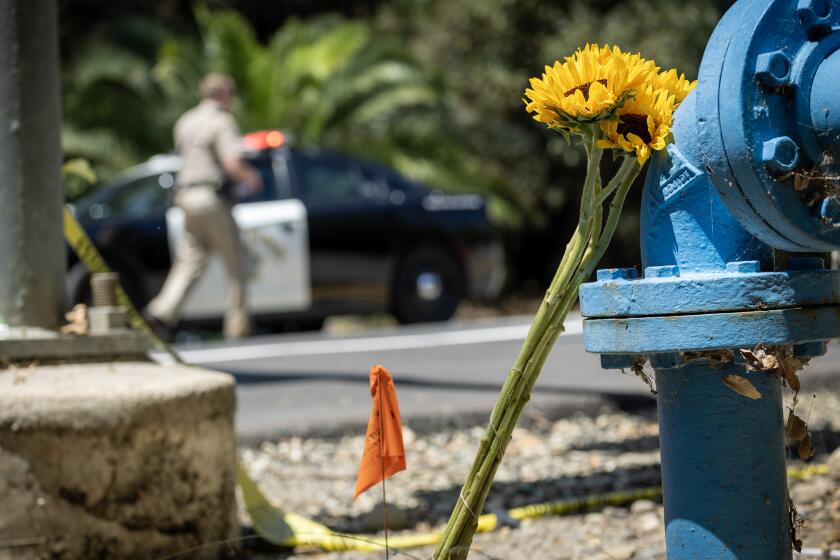 Trabuco Canyon, CA - August 24: A biker, who did not want to be identified, placed a bouquet of flowers in memorial for friends who were killed and injured at the edge of the crime scene along El Toro Road as Orange County Sheriff's deputy stands guard and investigators work the scene where a gunman killed three people and six were taken to hospitals after a shooting Wednesday night at Cook's Corner, a landmark biker bar at Cook's Corner in Trabuco Canyon Thursday, Aug. 24, 2023. An Ex-cop is the suspected gunman in mass shooting at O.C. biker bar, sources say; 4 dead, 6 injured. (Allen J. Schaben / Los Angeles Times)
