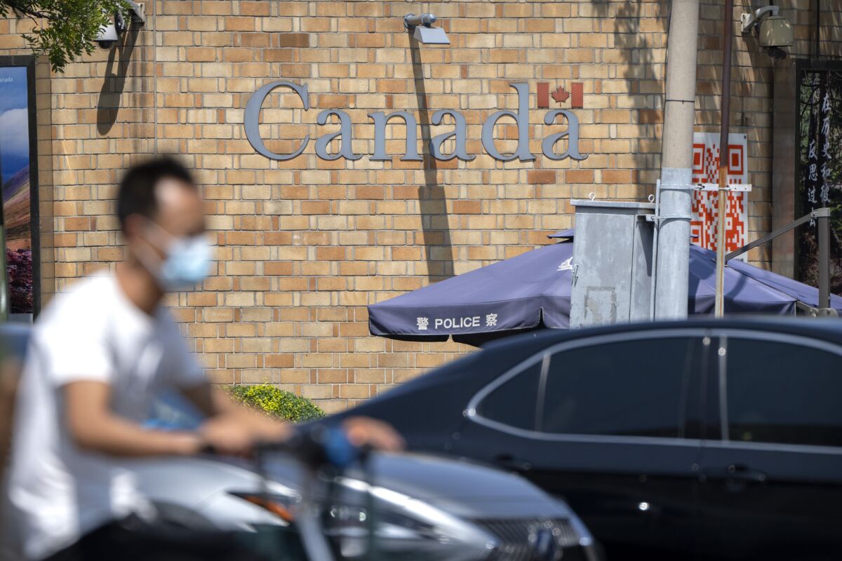 A man rides a scooter across an intersection near the Canadian Embassy in Beijing, Tuesday, Aug. 10, 2021. A Chinese court has rejected an appeal by a Canadian whose sentence in a drug case was increased to death after an executive of tech giant Huawei was detained in Vancouver. (AP Photo/Mark Schiefelbein)
