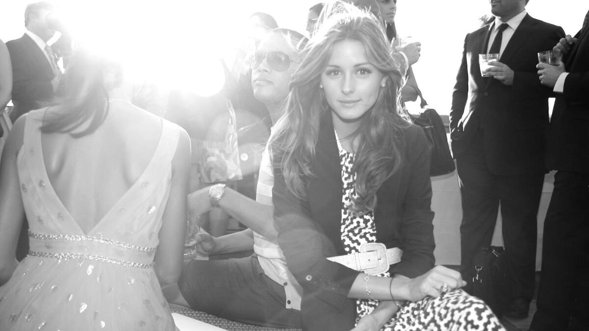 Olivia Palermo sits among a crowd while looking at the camera with a slight smile on her face