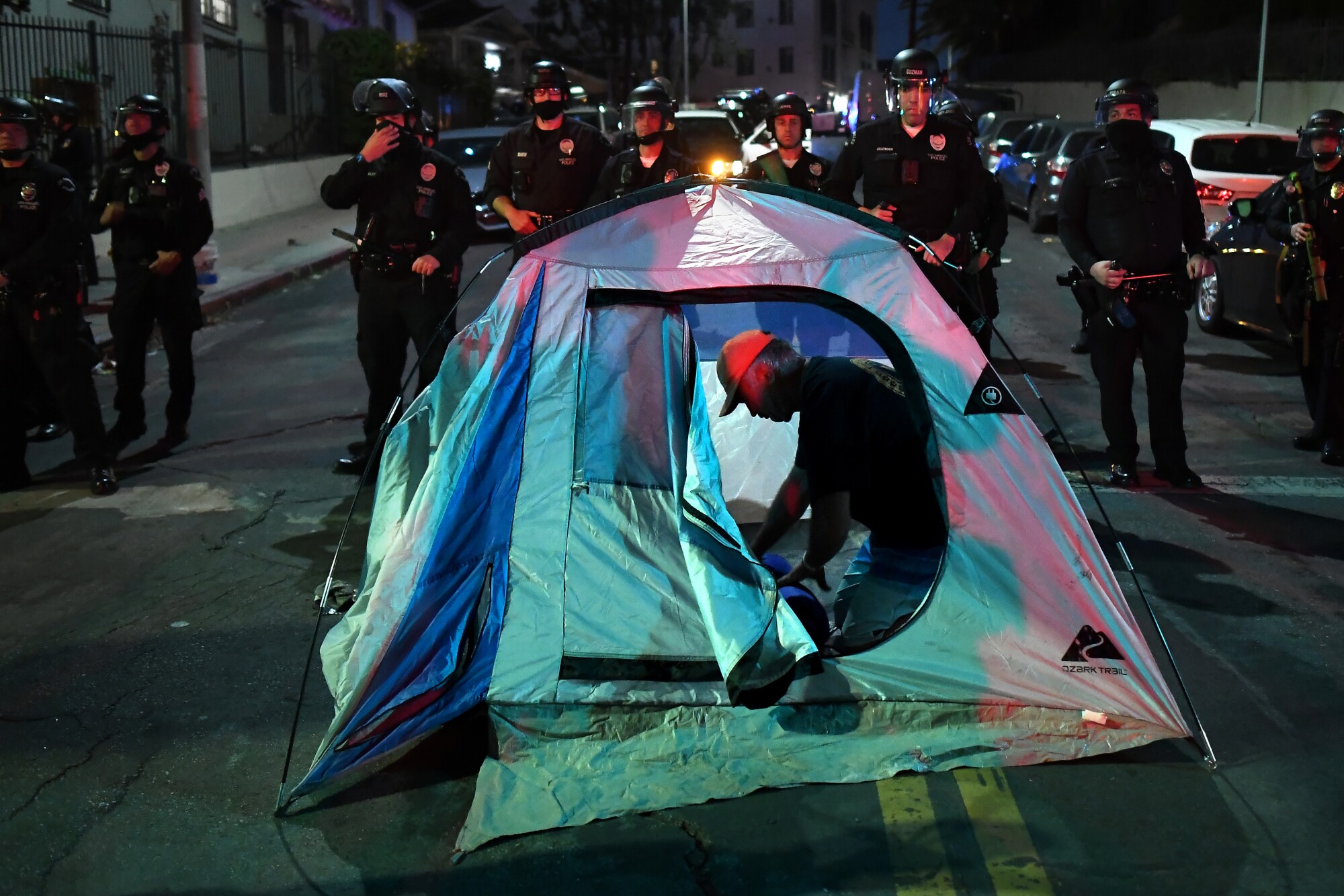 A protester sets up a tent as LAPD officers stand guard.