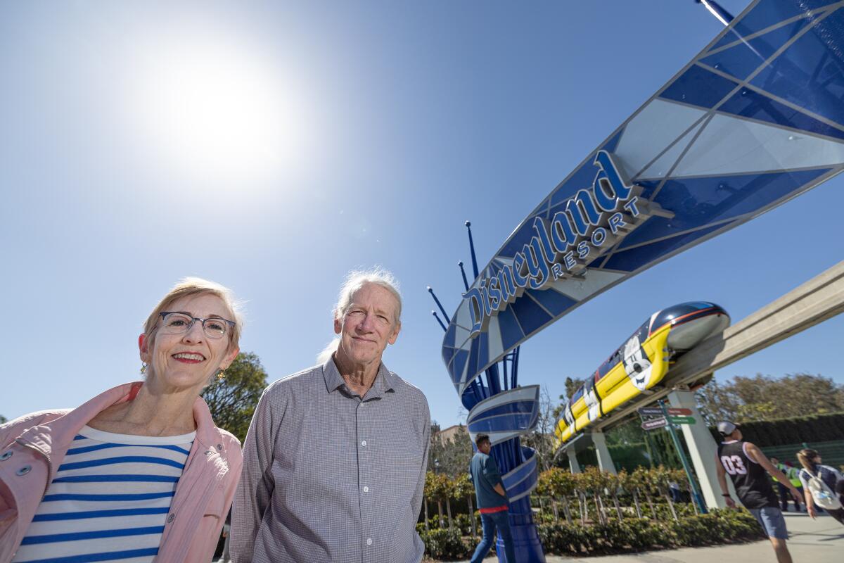 Climate activists Zan Dubin and Paul Scott stand near the entrance to Disneyland as the Monorail passes overhead.