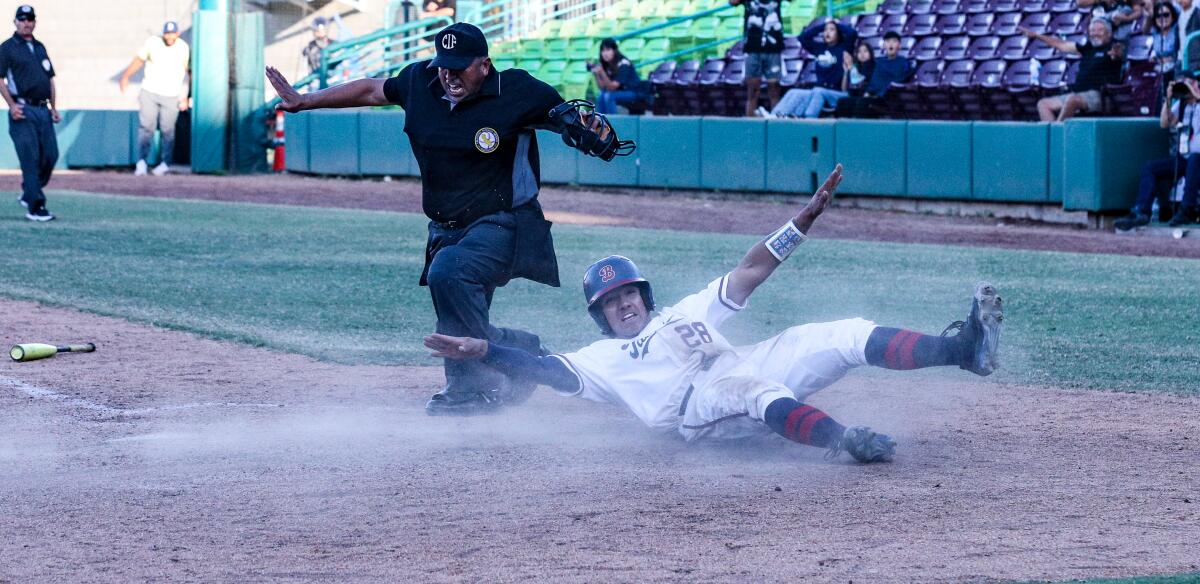 Isaiah Kapur of Beckman signals he's safe while sliding across home plate with the winning run against St. John Bosco.