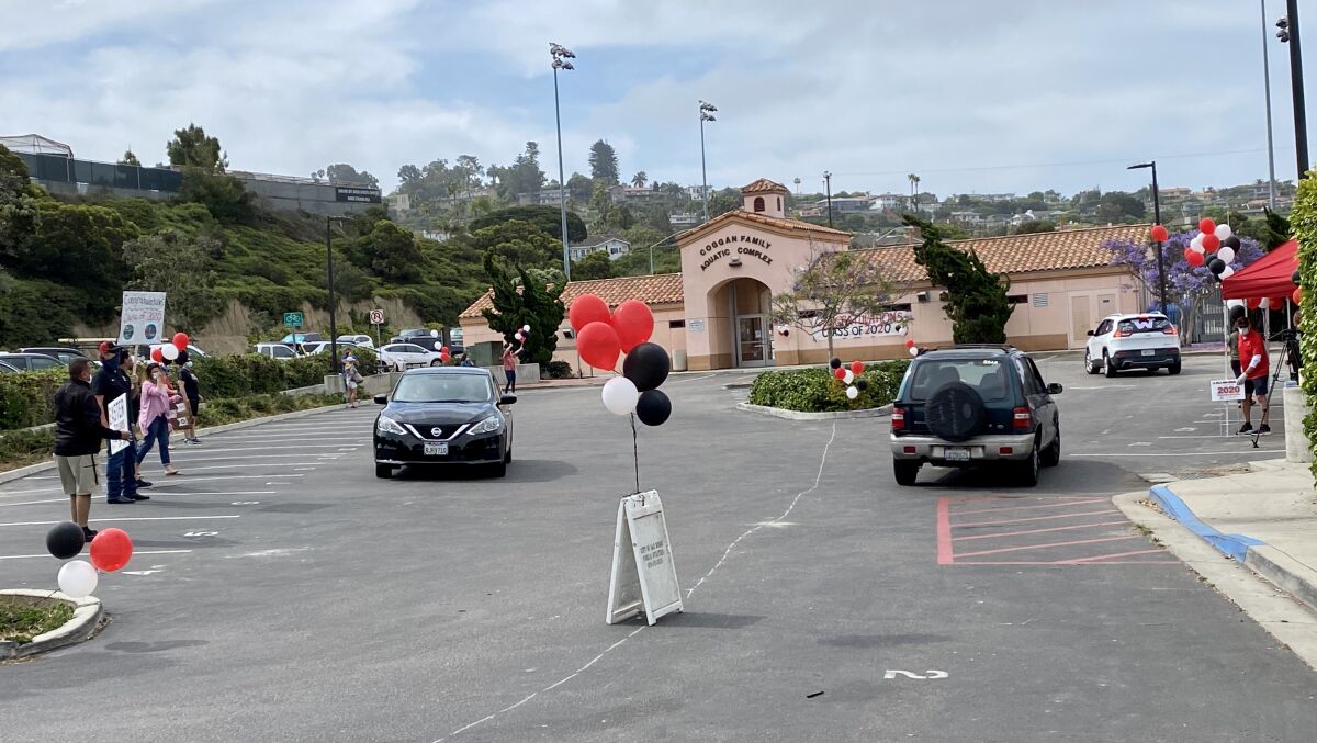La Jolla High staff and faculty with signs and balloons cheer for Class of 2020 seniors, accompanied by music from a DJ.