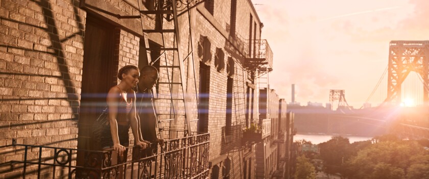 Leslie Grace and Corey Hawkins stand on a fire escape at sunset in the movie "In the Heights."
