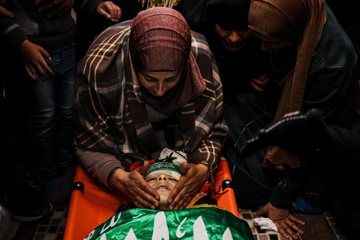 A woman puts her hands on her son's cheeks and bends over him during his funeral.