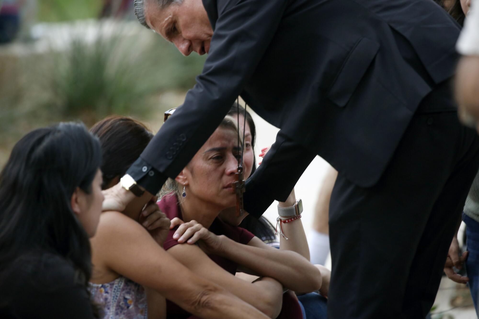 A man in a dark suit reaches out to several women who are upset