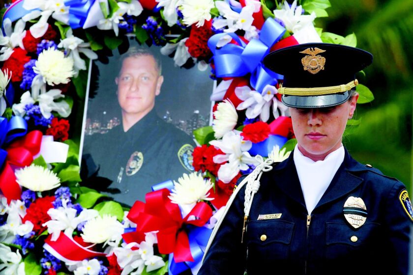 SDPD Officer Allyson Boyd stood in front of a wreath and photograph of slain officer Jeremy Henwood at the 28th annual Law Enforcement Memorial Ceremony Wednesday at the County Administration Center. JOHN GIBBINS • U-T