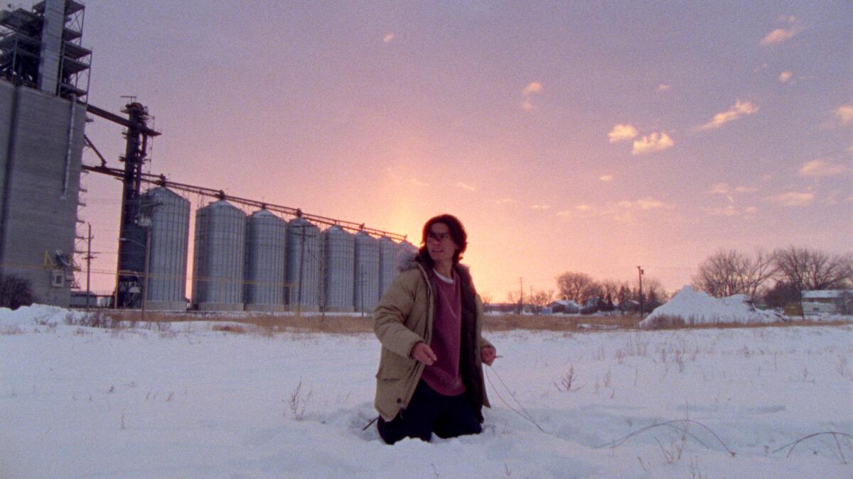 A person stands in snow up to their hips outside a power plant.