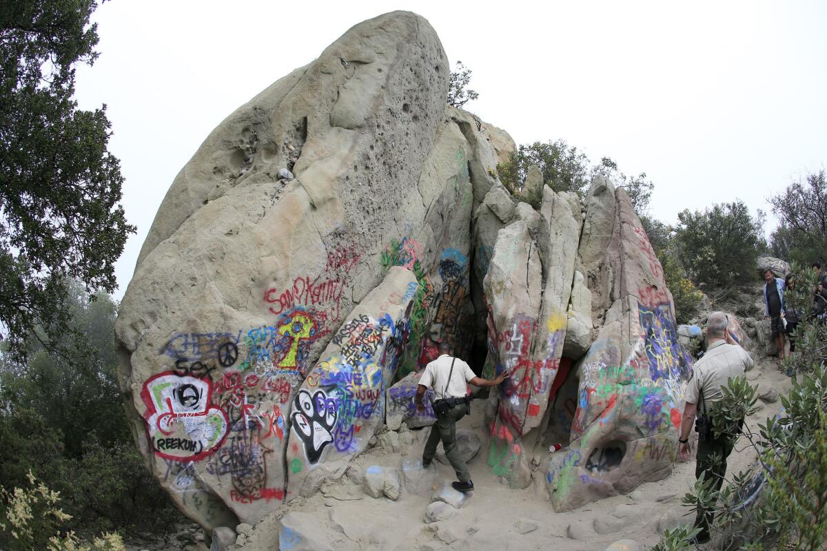 California State Park supervising ranger Lindsey Templeton, right, watches fellow ranger Dexter Crowder, center, enter the Corral Canyon Cave to cite one of a group of four artists for violation of a superintendent's closure order at Corral Canyon Cave.