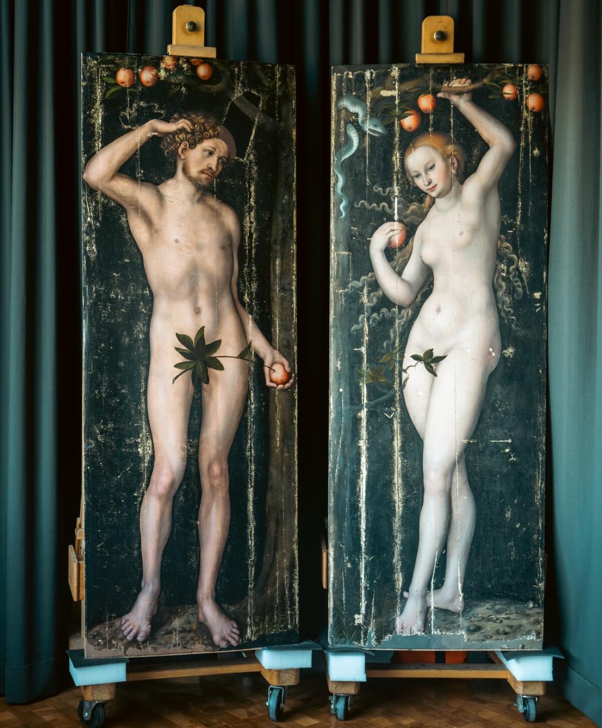 Two life-size panel paintings of naked Adam and Eve standing and holding apples. 