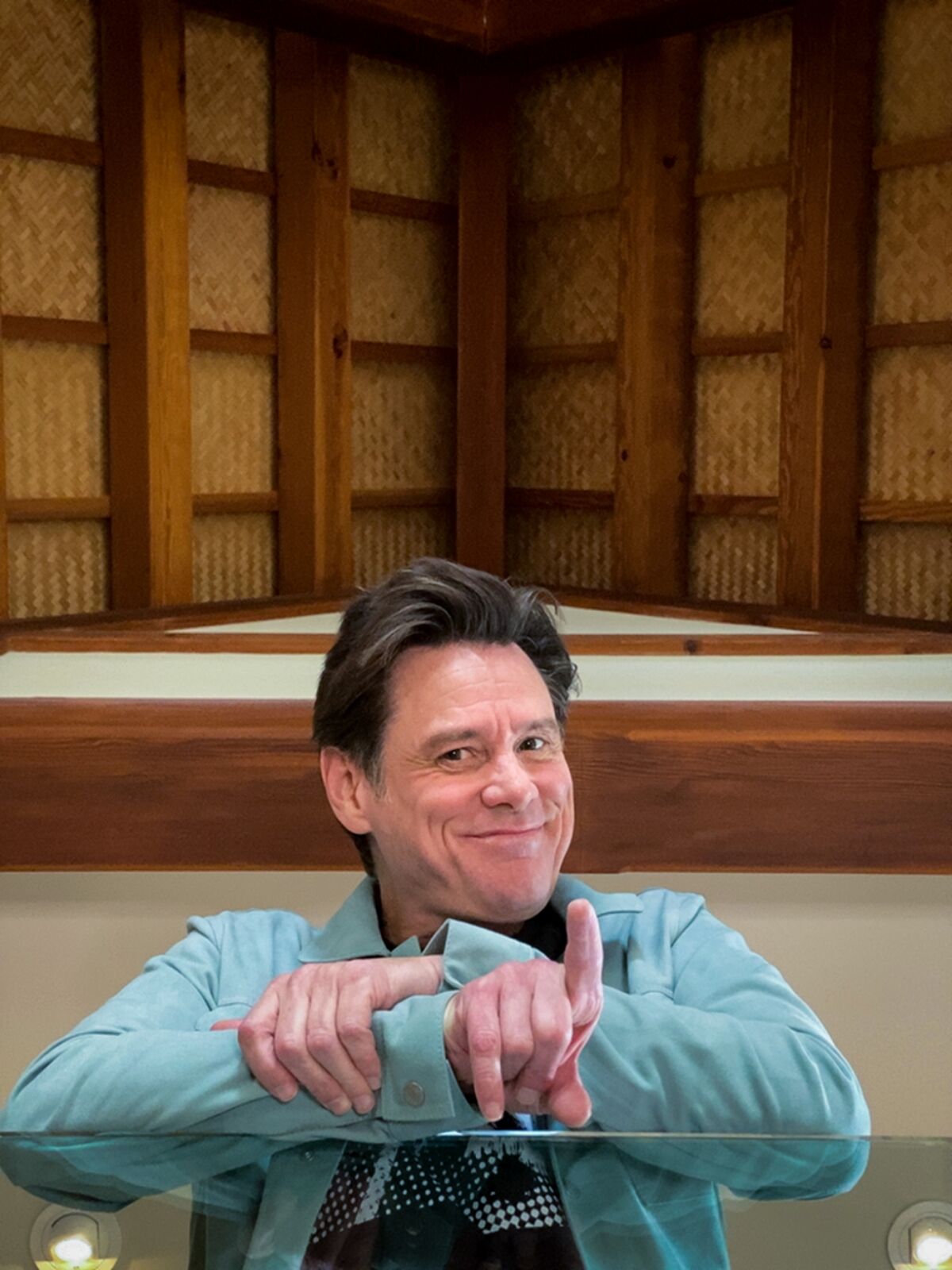 Jim Carrey in a blue button-up shirt, pointing his index finger upward